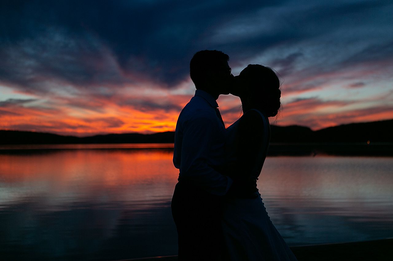 A silhouette of a bride and groom kissing with dramatic sunset colors of orange and pink in the background on Deer Lake in Boyne Falls, Michigan