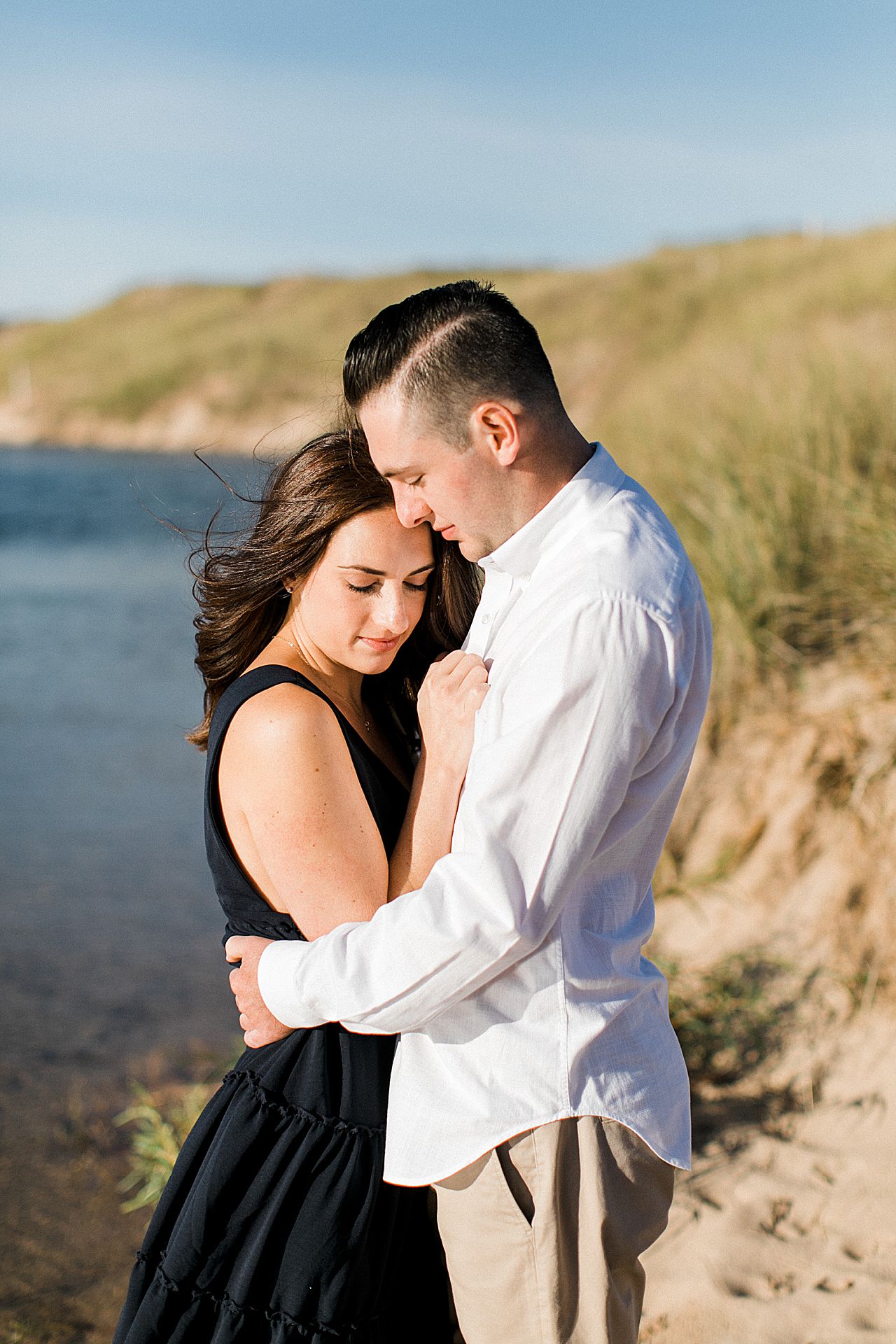 This is an engaged couple cuddling in the sun beside a lake in Michigan