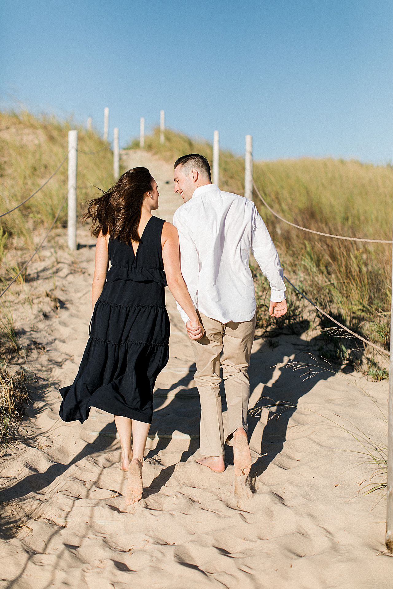 This is an engaged couple holding hands and walking up a sand dune in Michigan
