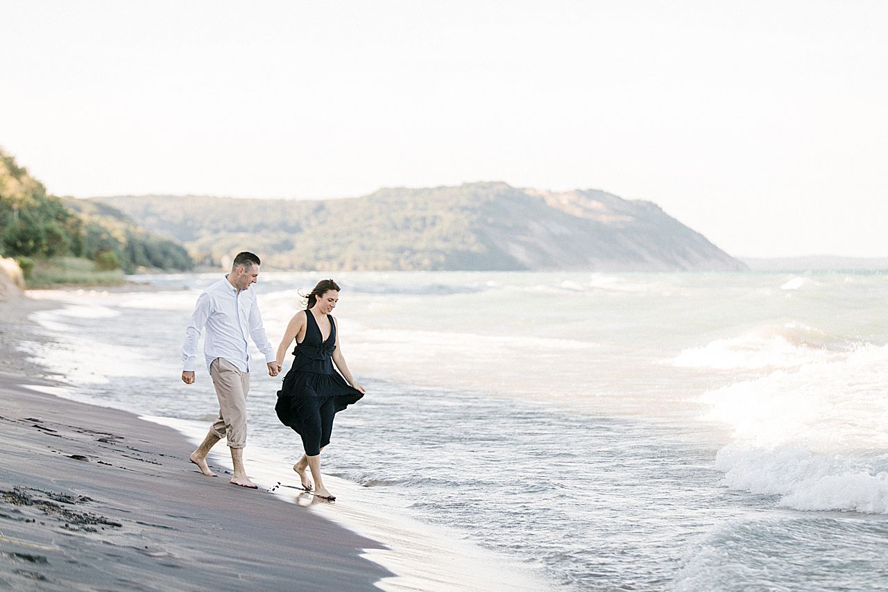 This is a couple holding hands and walking into Lake Michigan on a sunny day in Empire, Michigan