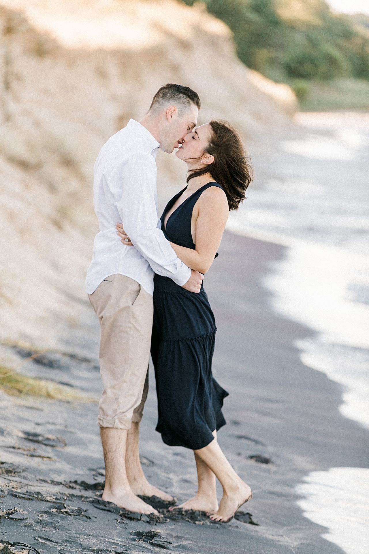 This is an engaged couple kissing along the lakeshore in Empire, Michigan