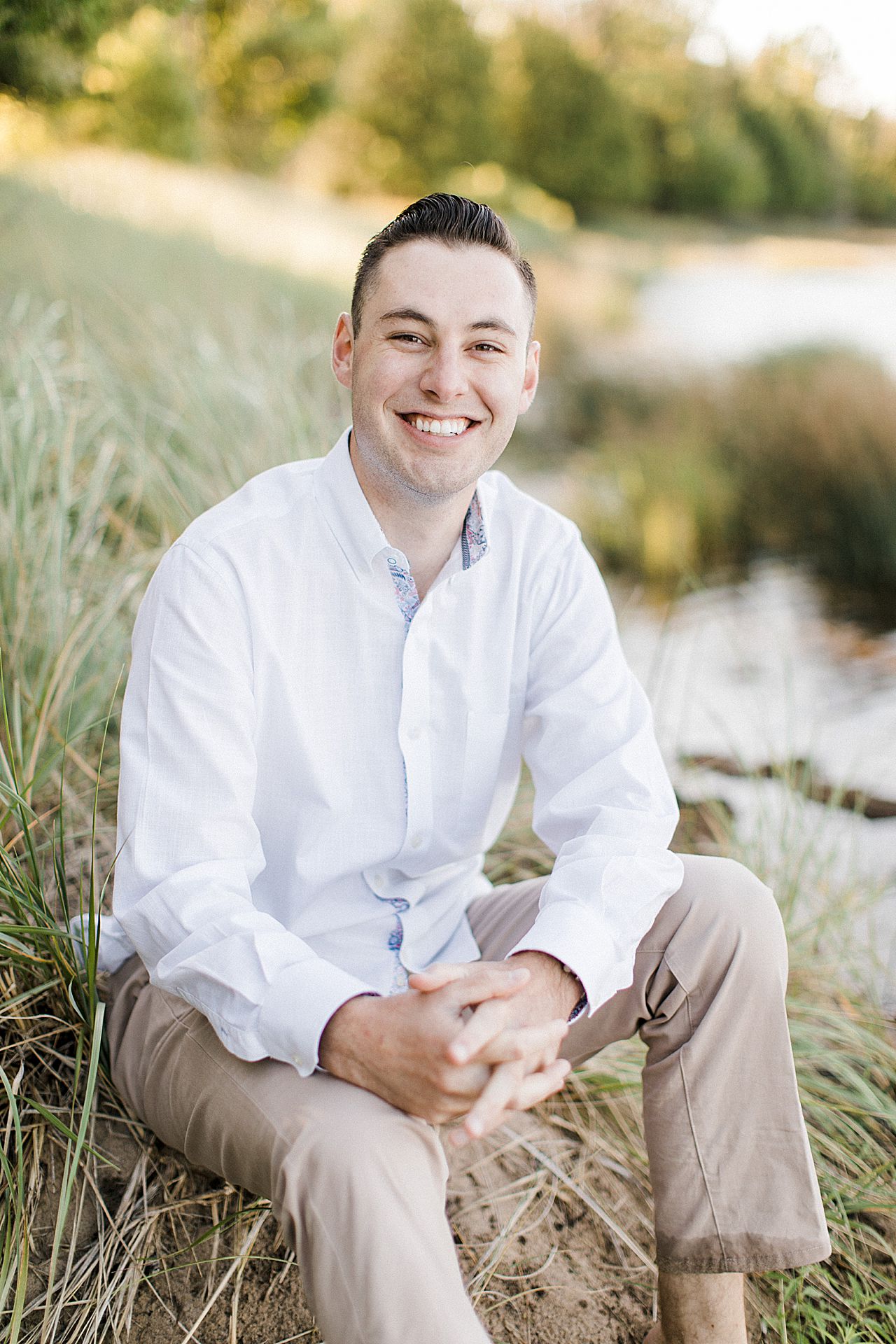 This is a portrait of a man sitting in a grassy sand dune and smiling in Empire, Michigan