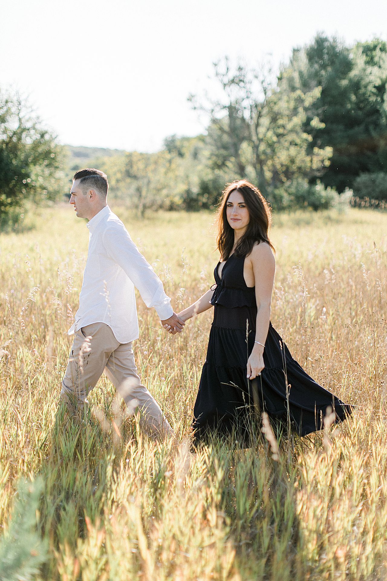 This is a portrait of a couple walking in a grassy field on a sunny day in Sleeping Bear Dunes National Lakeshore