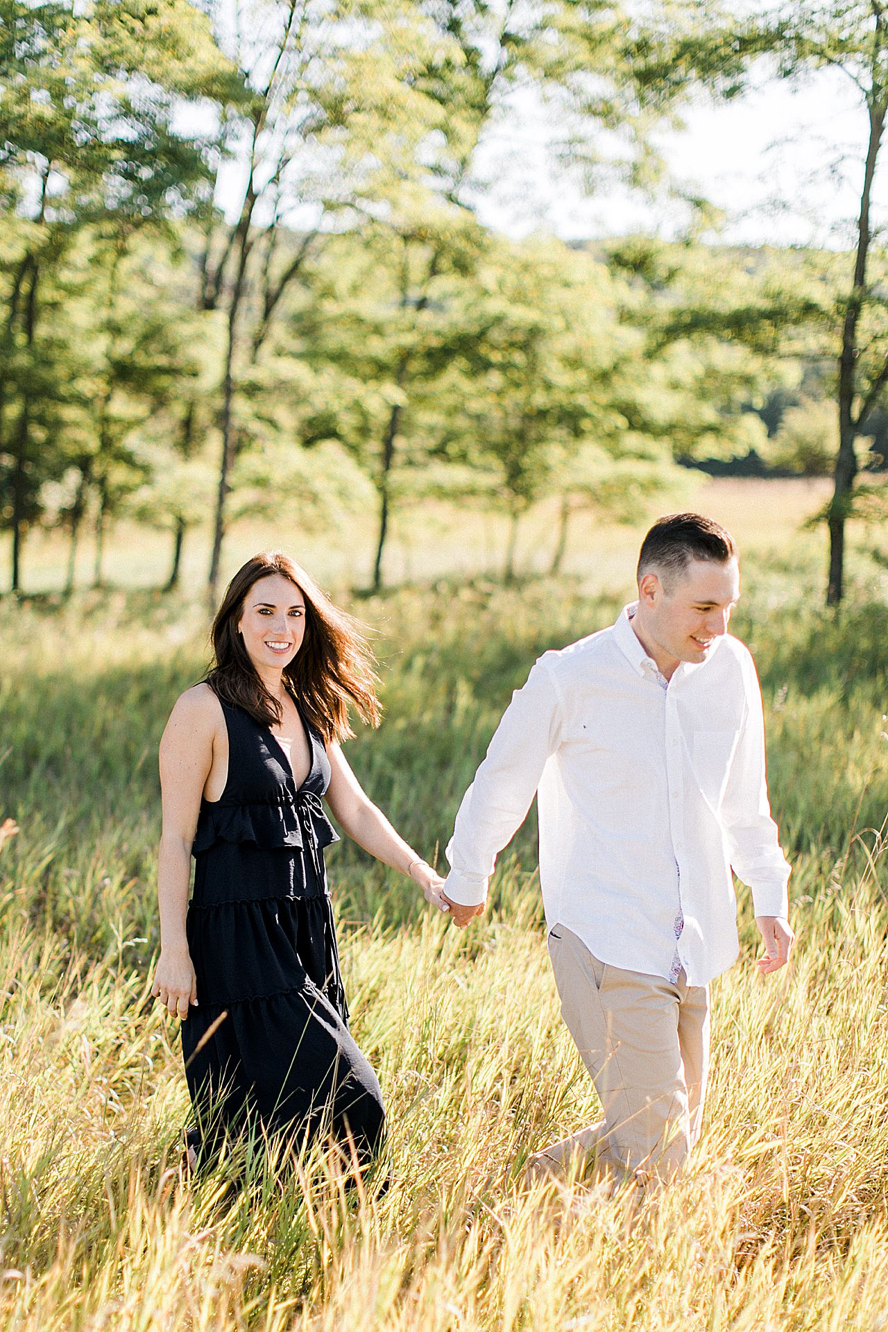 This is a portrait of a couple holding hands and walking in a grassy field on a sunny day in Northern Michigan