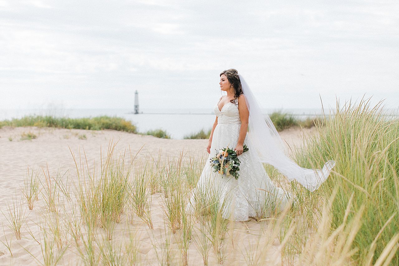 A bride on the beach in Frankfort, Michigan by Lake Michigan and a lighthouse