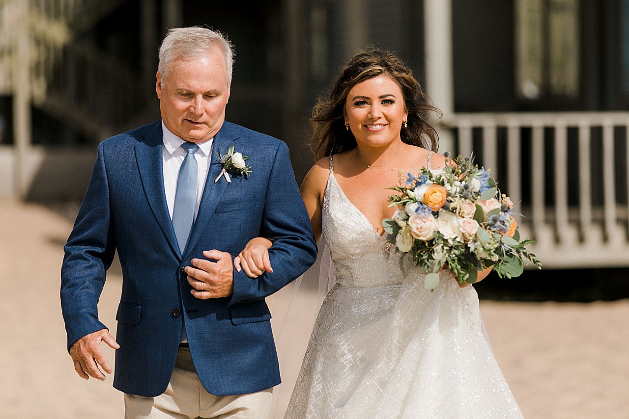 A bride and her father walking down the aisle at a wedding ceremony on a beach in Frankfort, Michigan
