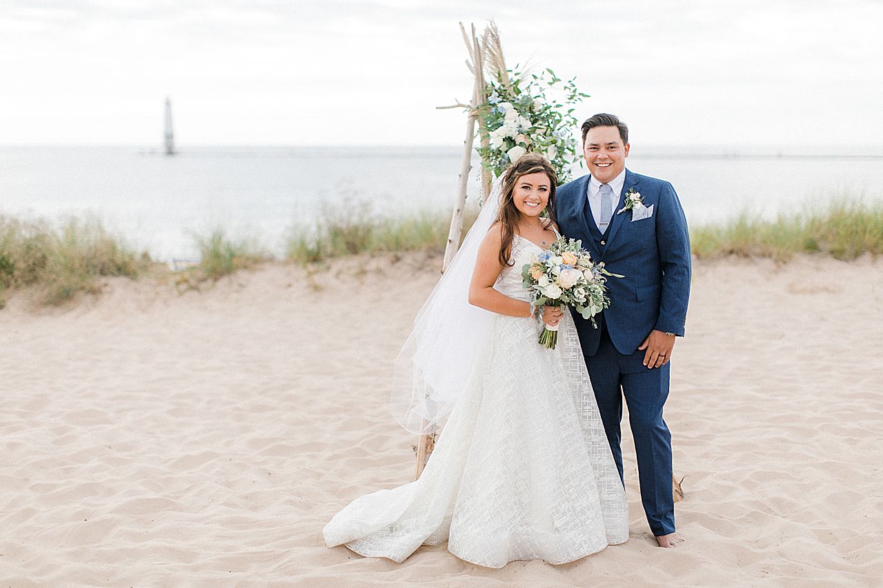 A bride and groom by their ceremony driftwood arch by Lake Michigan in Frankfort, Michigan