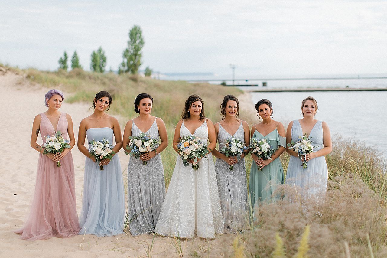 A bride and bridesmaids on the beach along Lake Michigan in Frankfort, Michigan with a lighthouse in the background