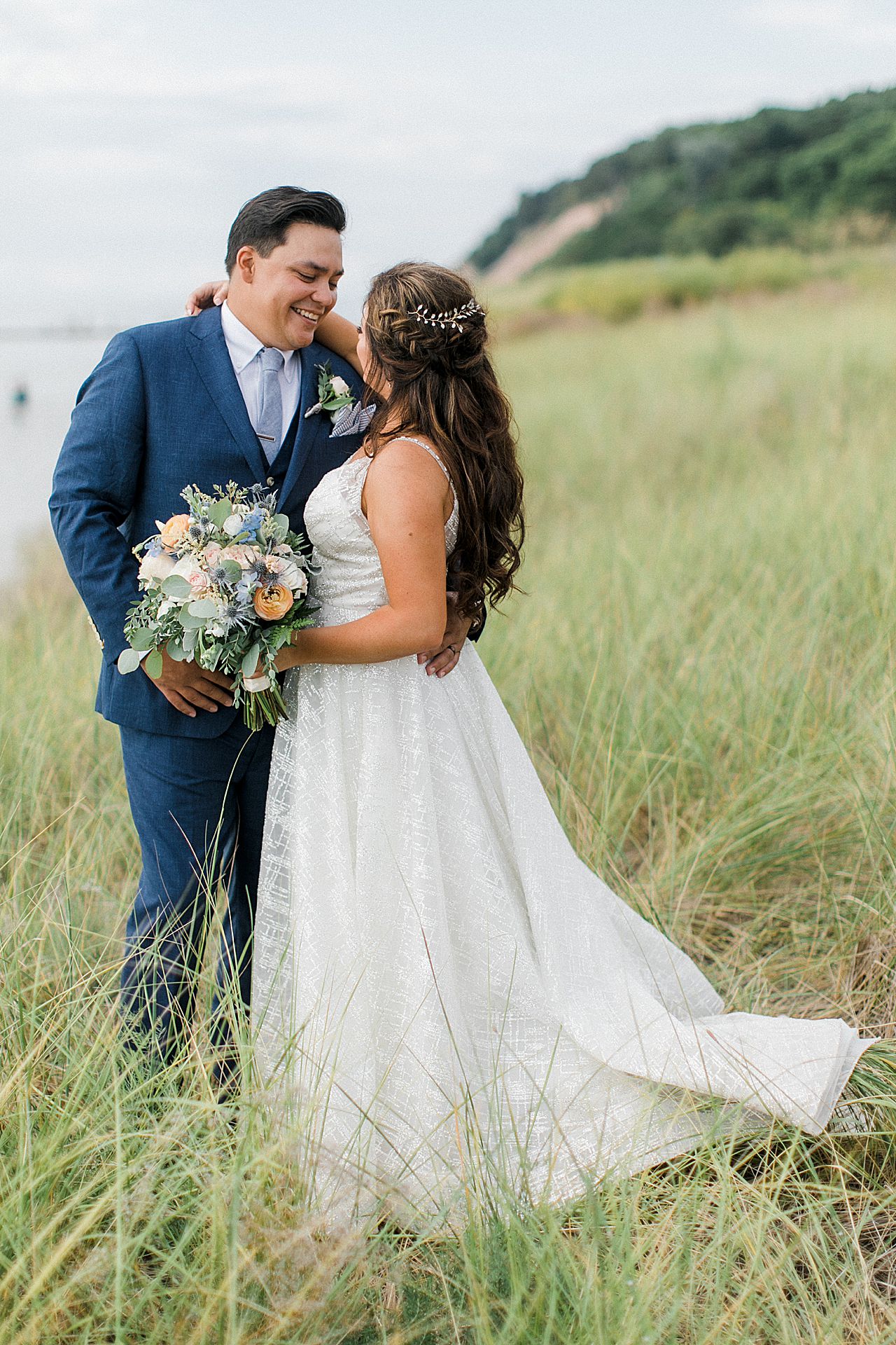 A bride and groom laughing in dune grass on the beach along Lake Michigan in Frankfort, Michigan