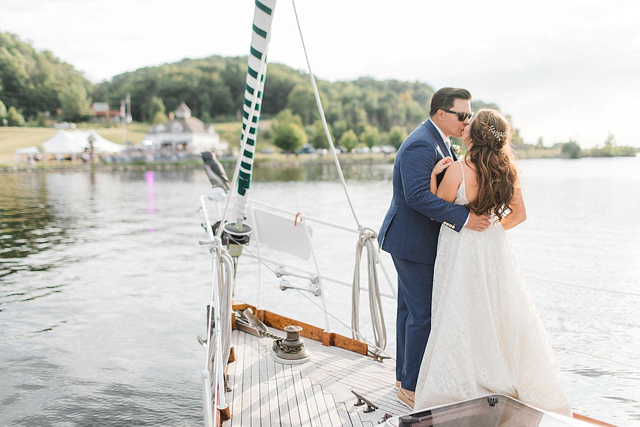 A bride and groom kissing on a sailing boat while approaching their wedding reception in Elberta, Michigan