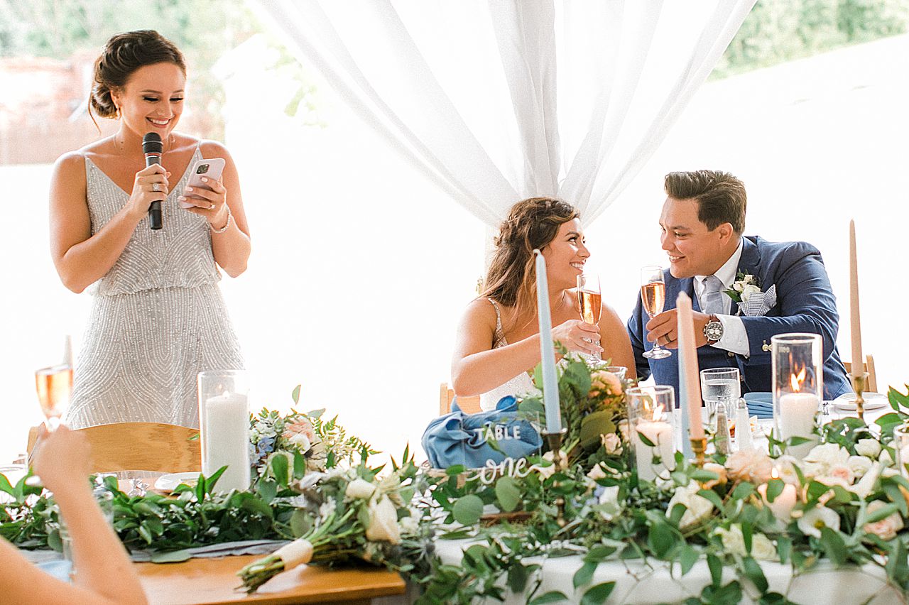 A bride and groom clinking their champagne glasses during the maid of honors speech