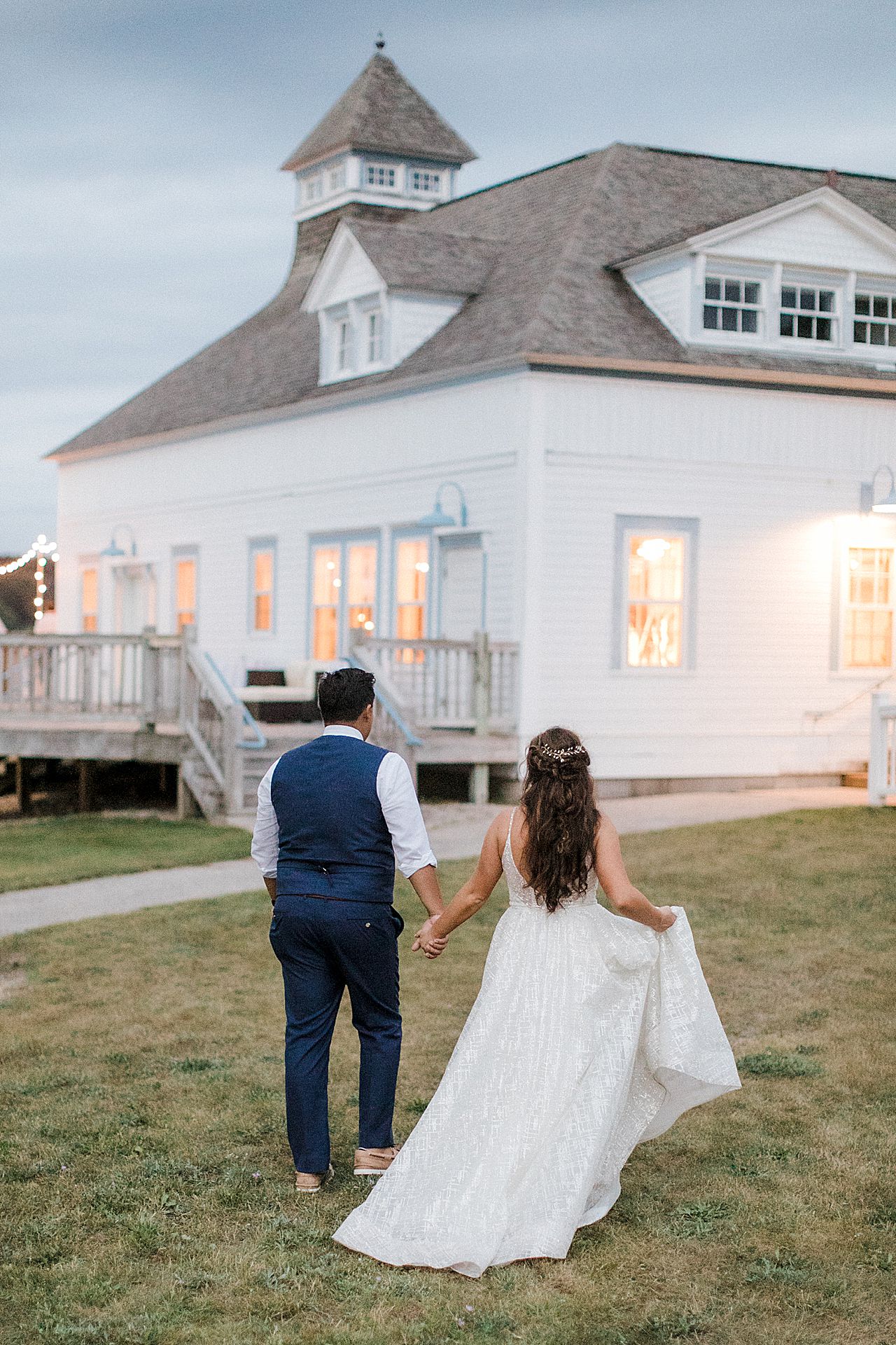 A bride and groom walking together while holding hands in front of the Elberta Life Saving Station at dusk