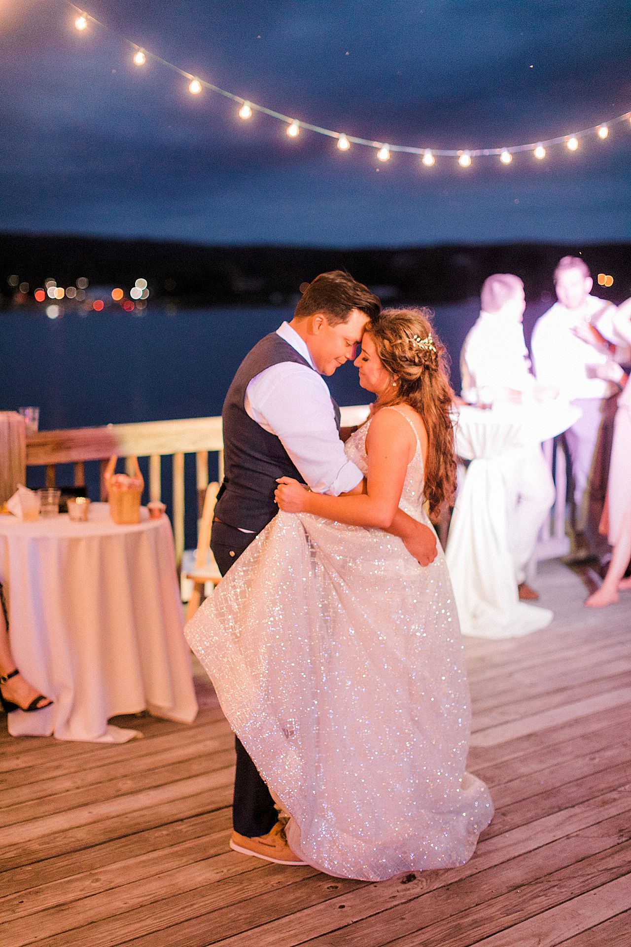 A bride and groom dancing on the deck of the Elberta Life Saving Station with lights strung over their heads
