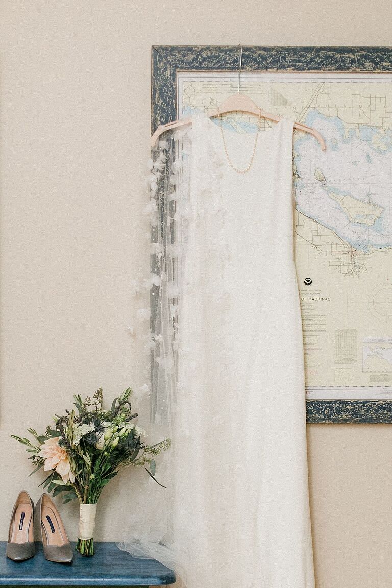 A white wedding dress hung up on a large framed map of Michigan with shoes and a bouquet
