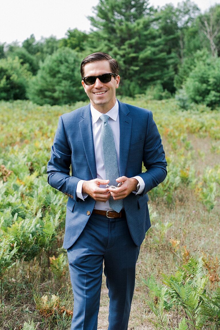 A groom walking through a field with a blue suit