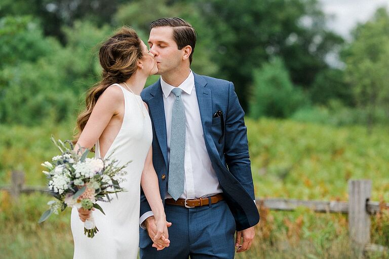 A bride and groom kissing while walking at Houdek Dunes Natural Area in Michigan