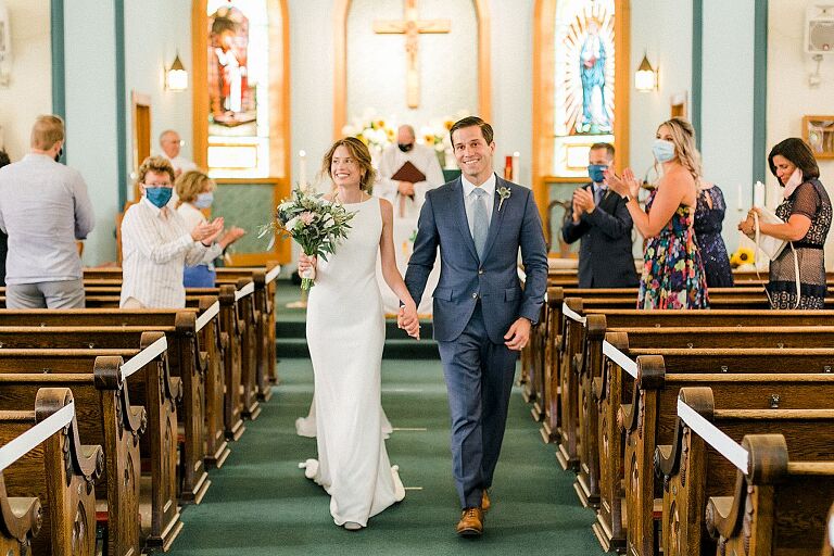 A bride and groom walking down the aisle while holding hands and smiling at their wedding ceremony in Leelanau County, Michigan