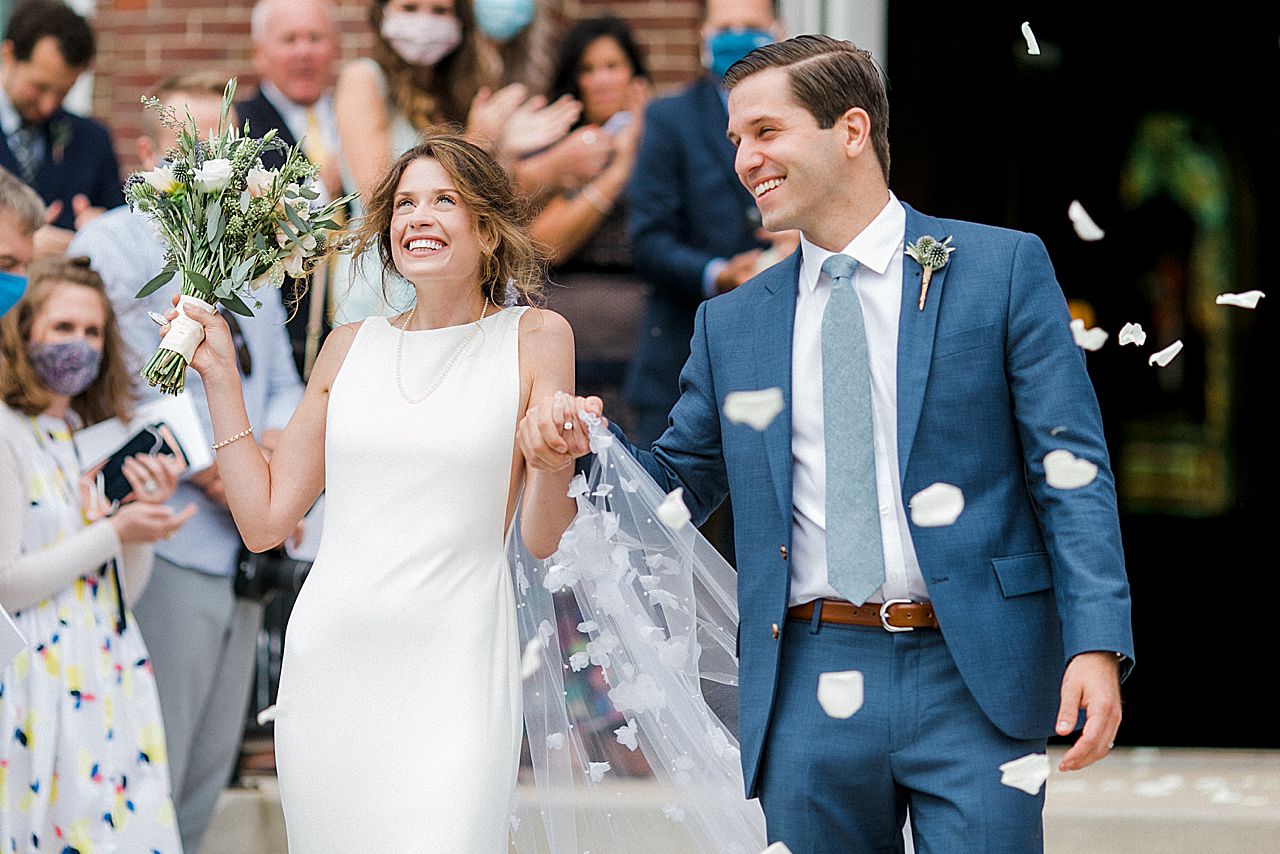A bride and groom walking out of St Wenceslaus catholic church in Leelanau County, Michigan while guests throw rose pedals