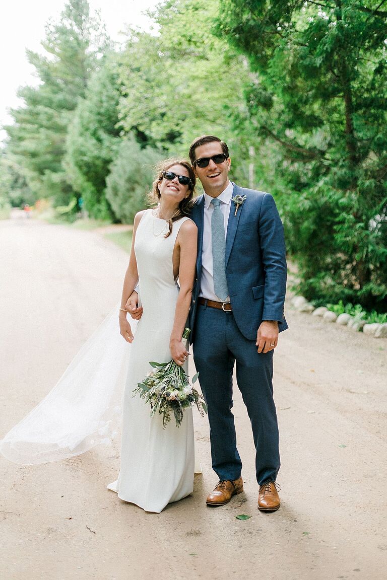 A bride and groom portrait of them smiling and wearing their sunglasses on a dirt road