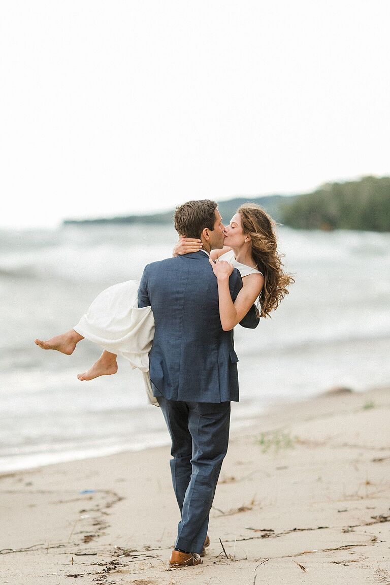 A groom carrying his bride down the lakeshore and kissing in Northport, Michigan