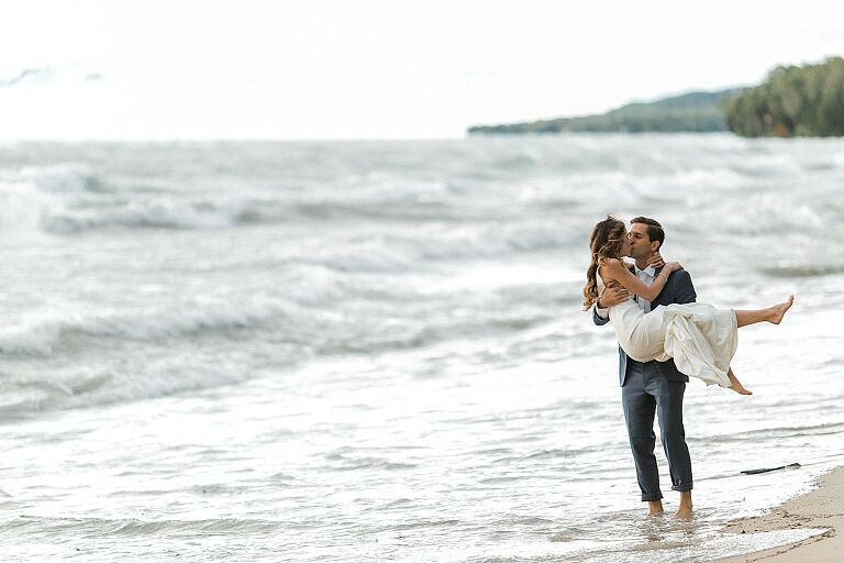 A groom holding his bride and kissing her with Lake Michigan in the background