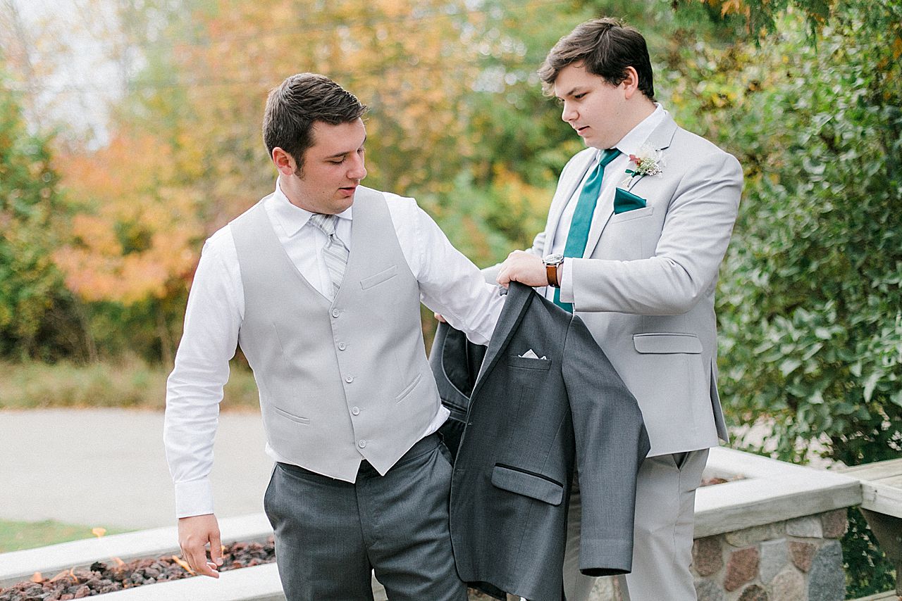 A groom putting on his jacket with the help of a groomsmen in Charlevoix, Michigan