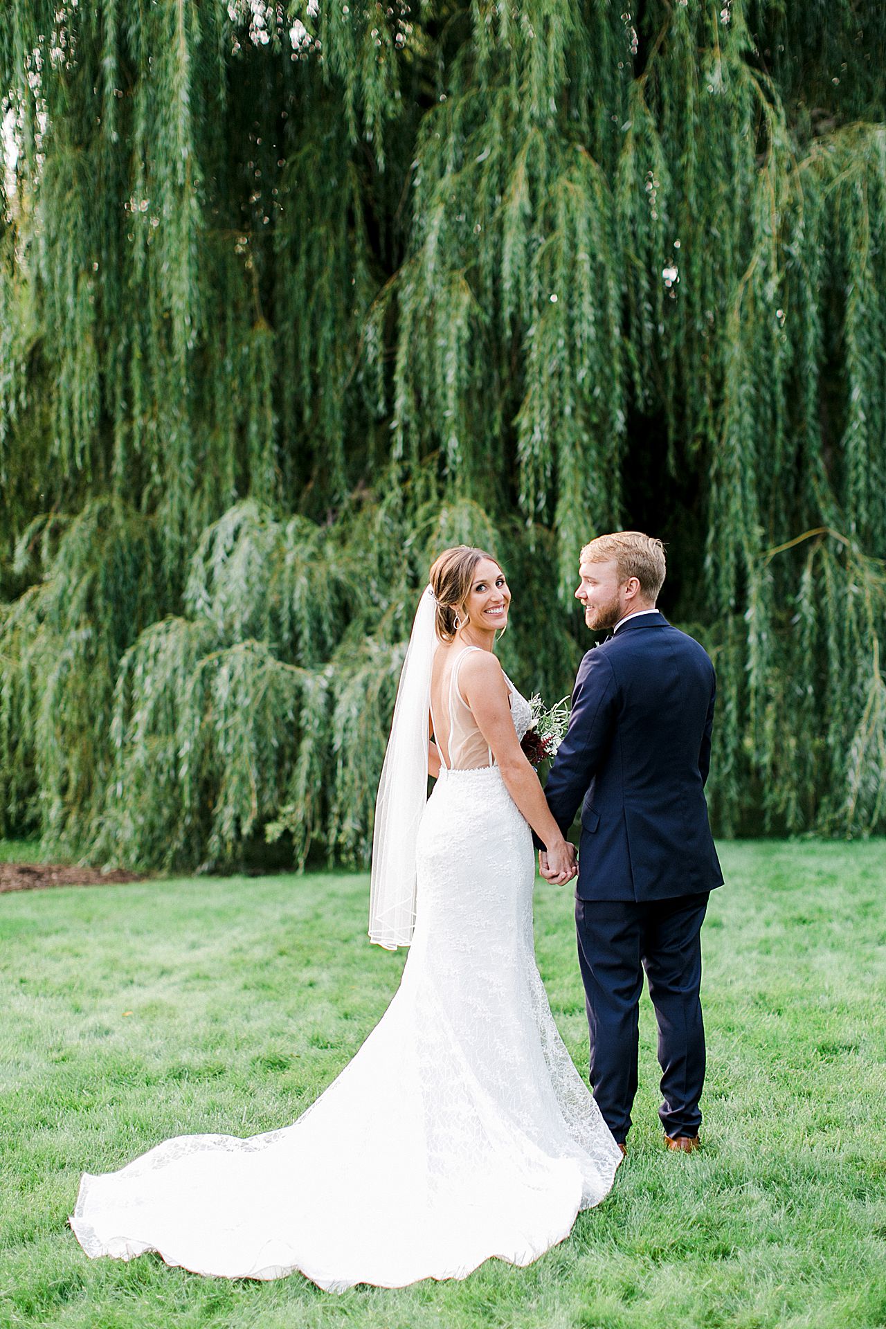 A bride looking back at the camera and smiling while holding her grooms hand