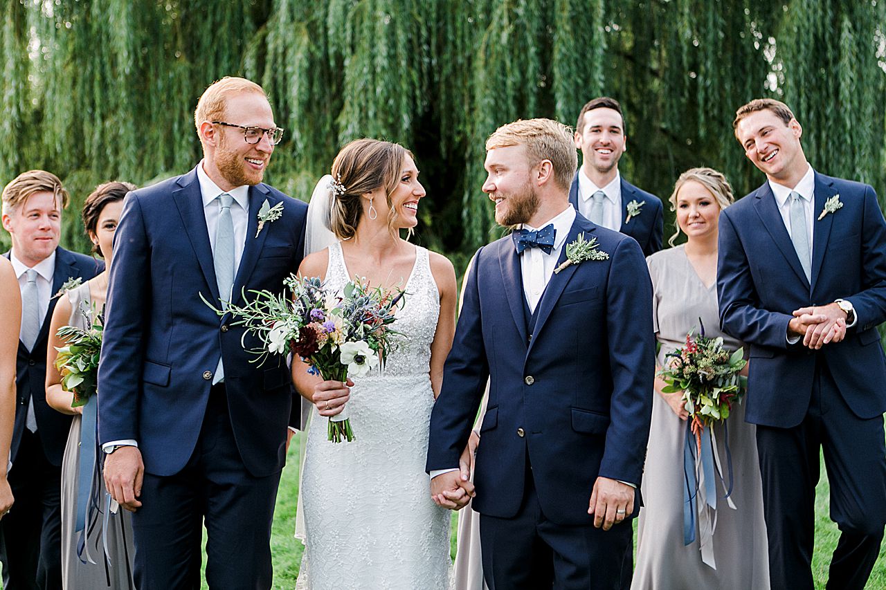 A bride and groom smiling at each other while walking with their wedding party in Northern Michigan