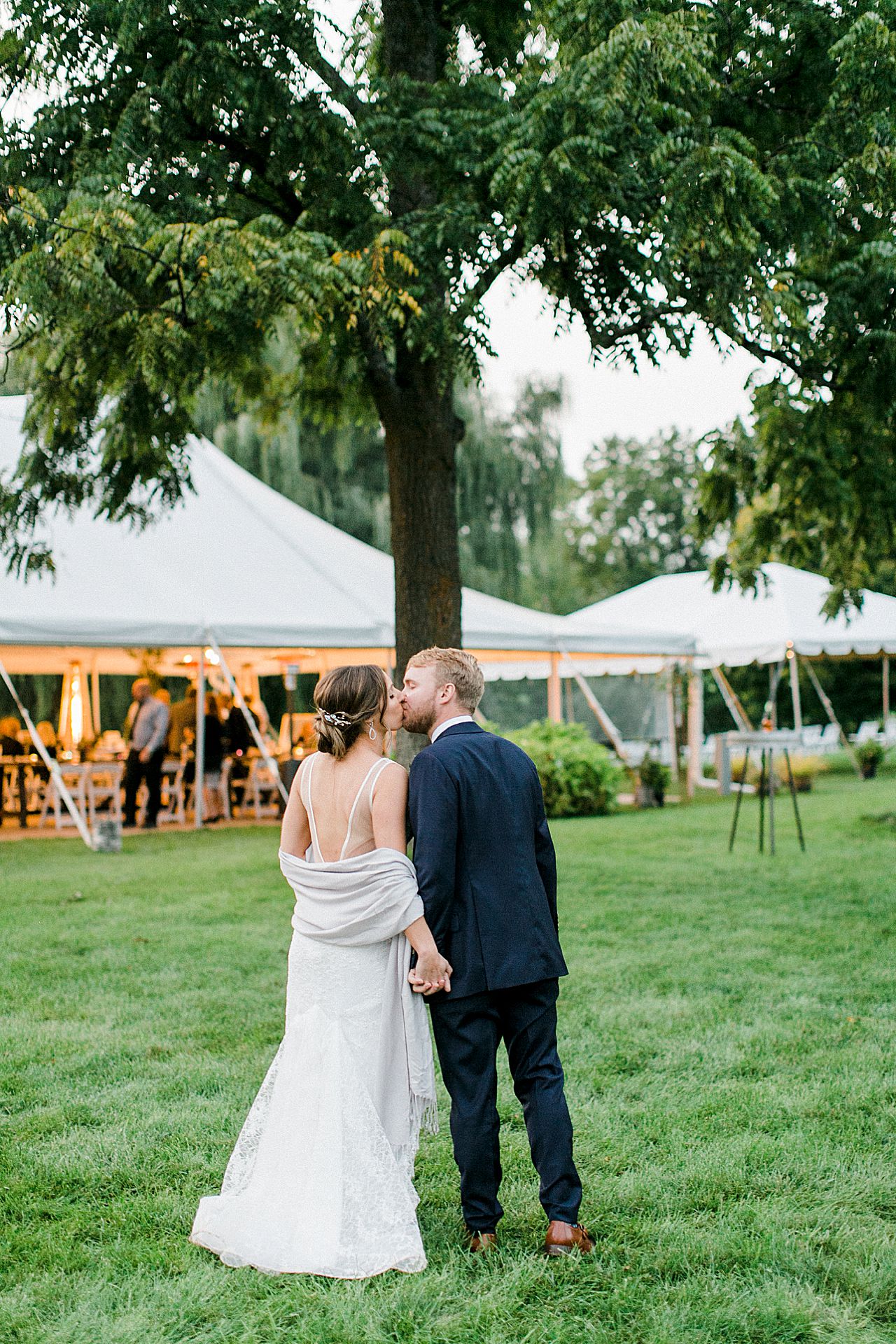 A bride and groom walking towards the reception tent and kissing