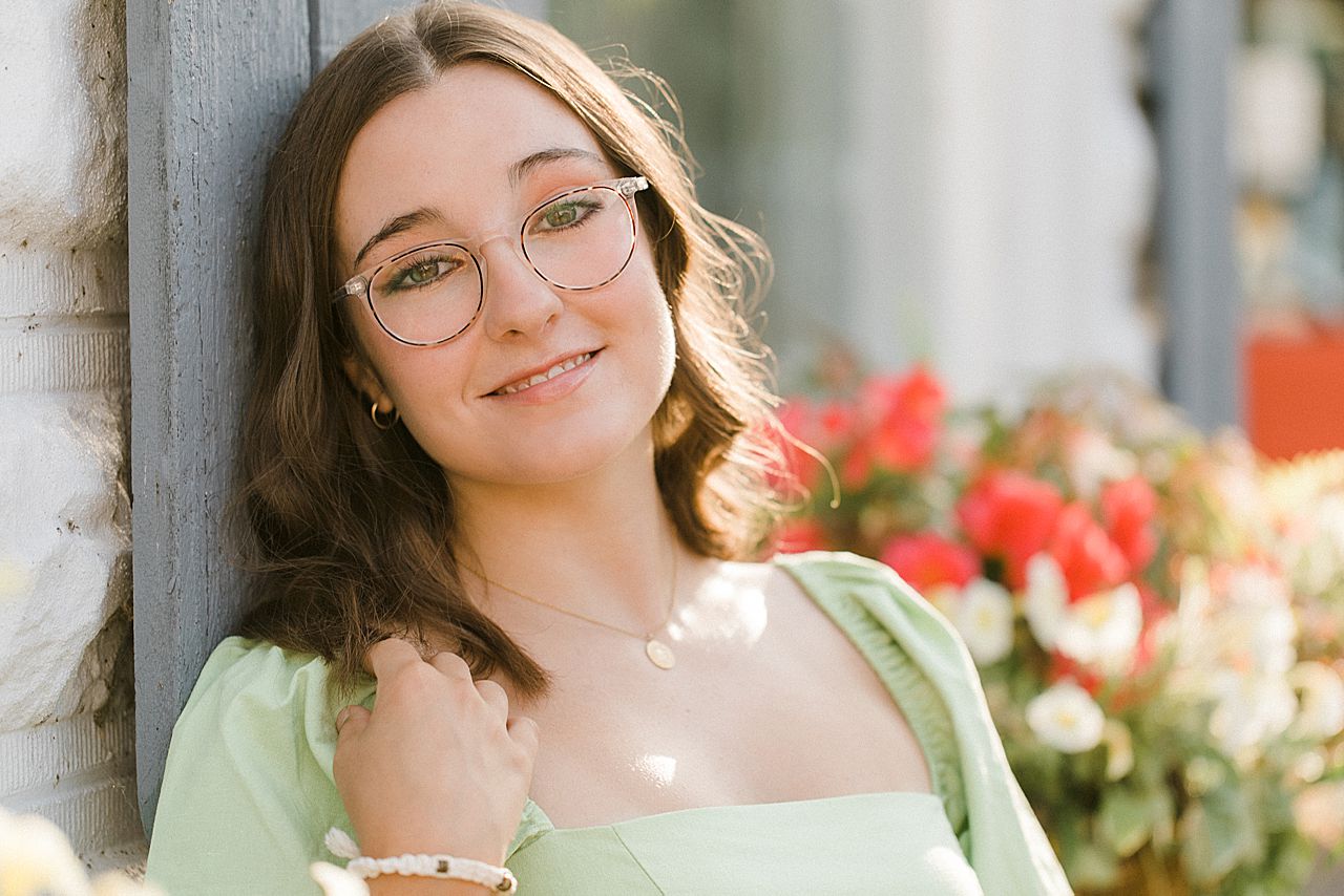 A girl smiling in a green dress and glasses during her senior portrait session in Charlevoix, MI