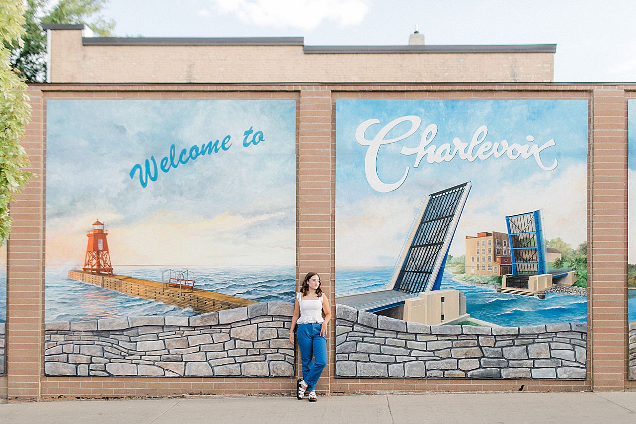 A girl wearing a white top and blue pants in downtown Charlevoix by a mural