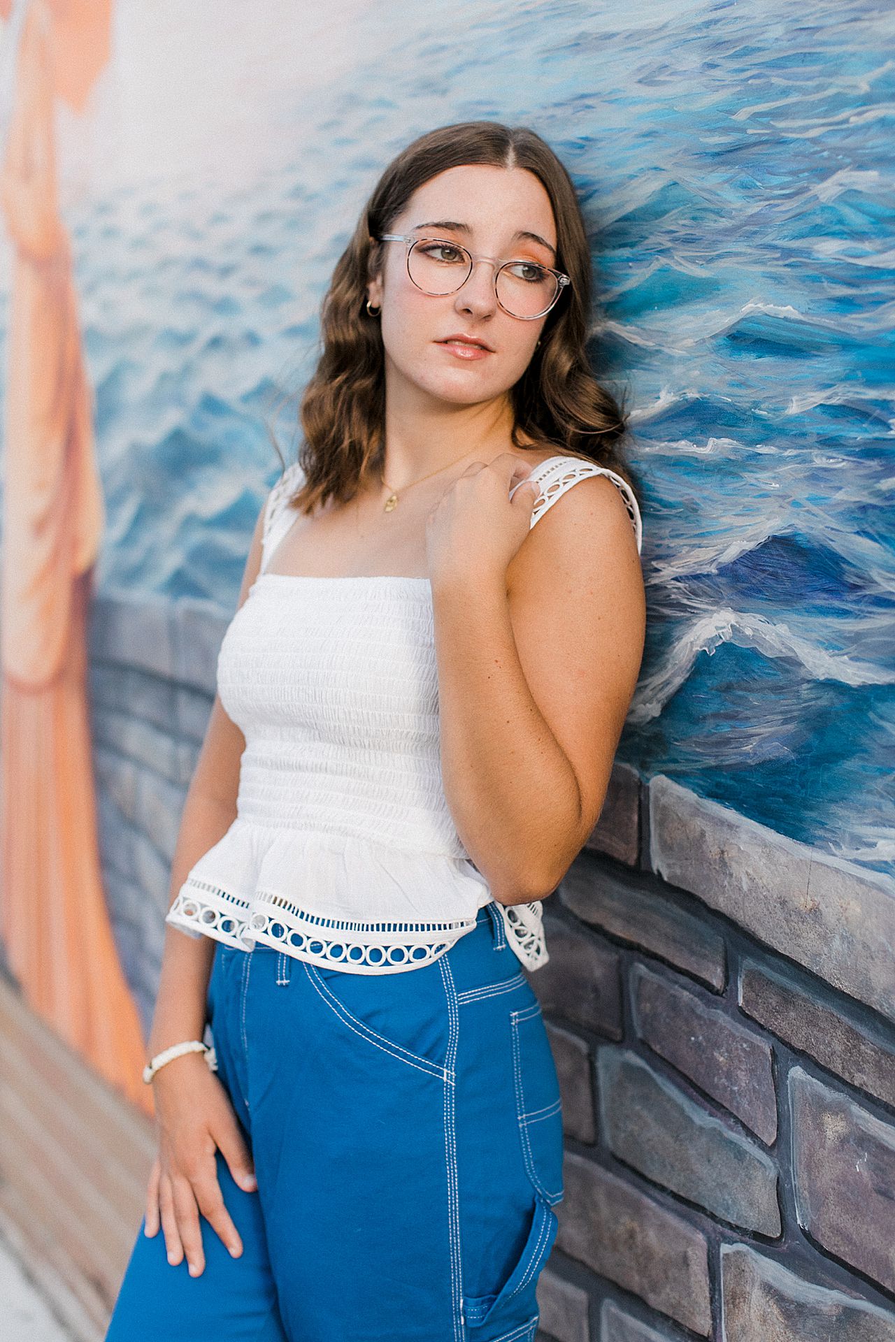 A girl wearing a white top and blue pants in downtown Charlevoix by a mural