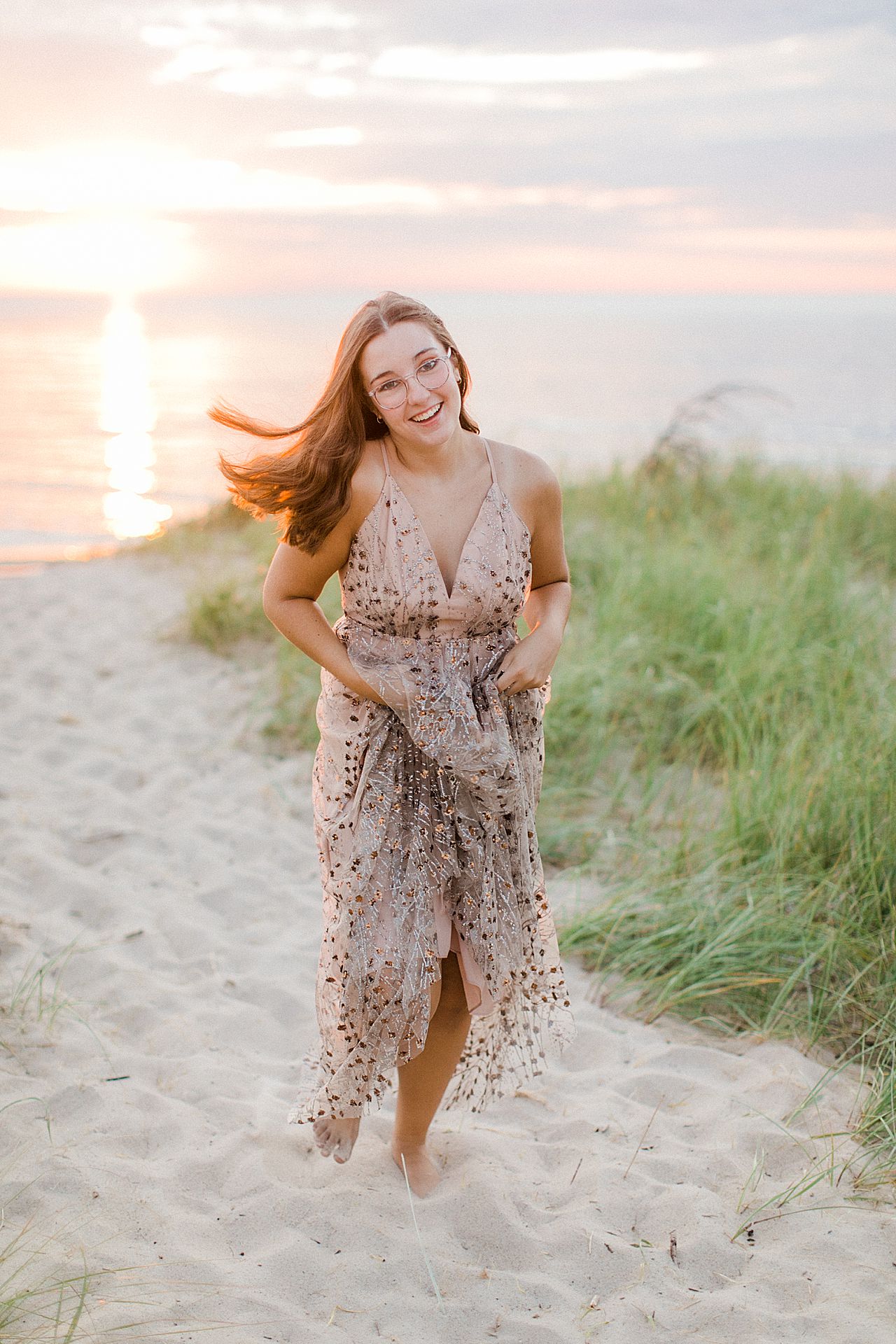 A senior portrait session with a girl running through sand dunes at sunset in Charlevoix, Michigan