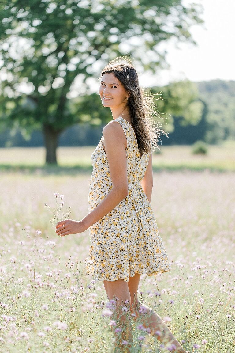 A girl wearing a yellow floral dress during her senior portrait session on a sunny evening in a field in Empire, Michigan