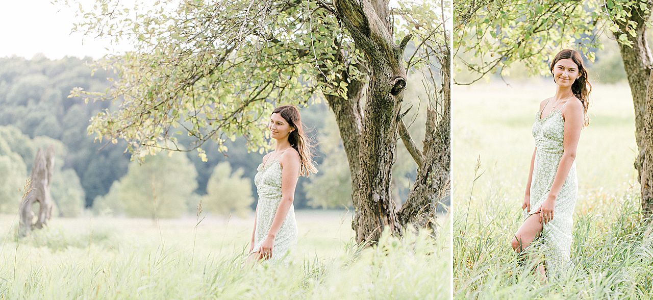 A girl taking senior portraits by a tree in a field in a light green dress during her senior portrait session