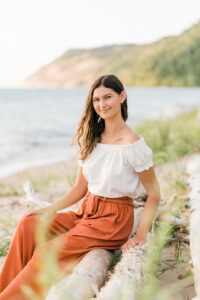 A girl sitting onsite logs near Lake Michigan with Sleeping Bear Dune National Lakeshore in the background