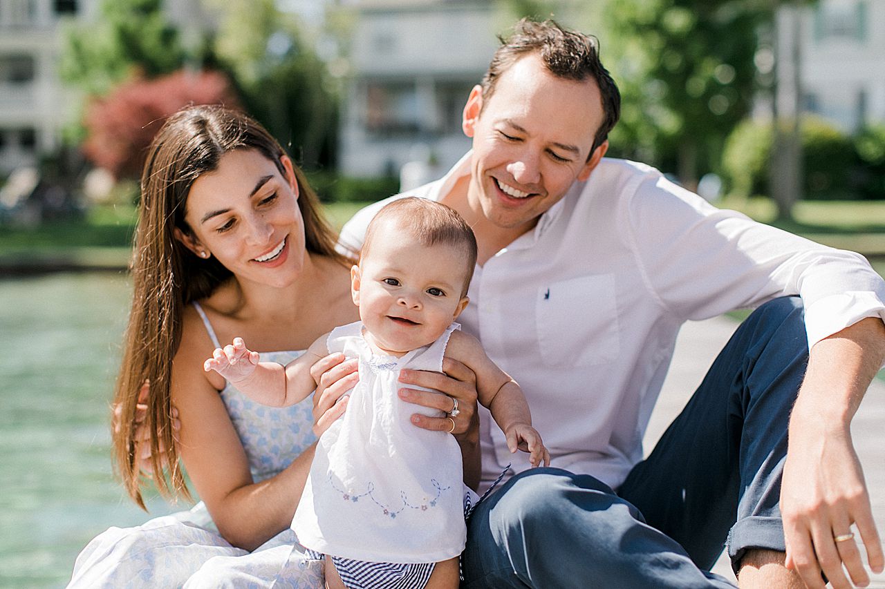 A baby girl smiling and holding her parents hands in Harbor Springs, Michigan