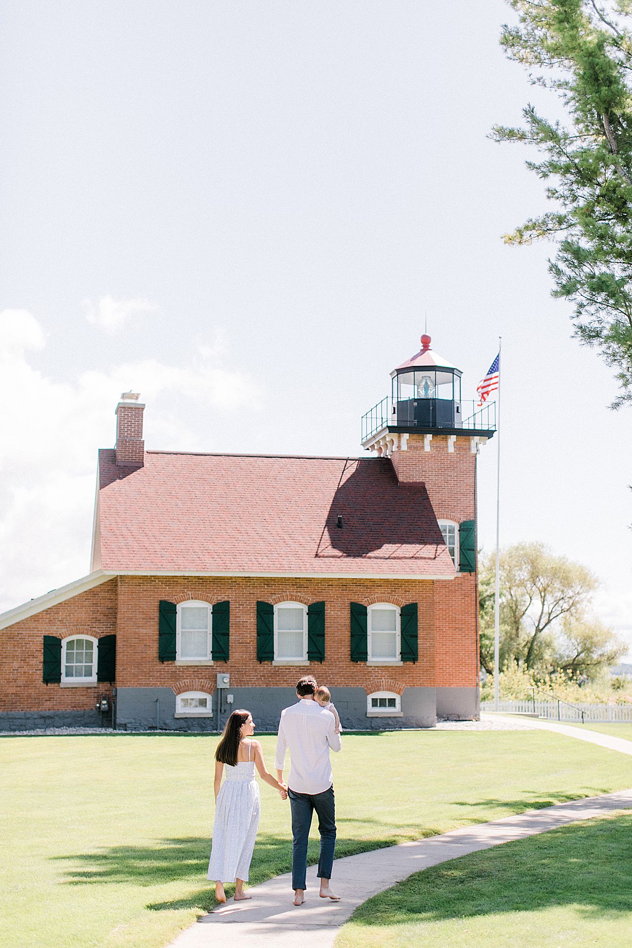 A family of three walking by the Harbor Point lighthouse in Harbor Springs, Michigan