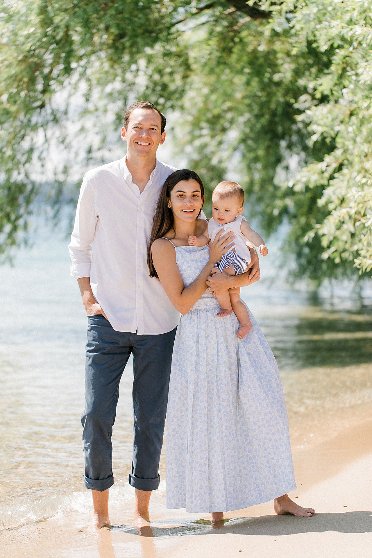 A family of three taking portraits by the lakeshore and a willow tree in Harbor Springs, Michigan