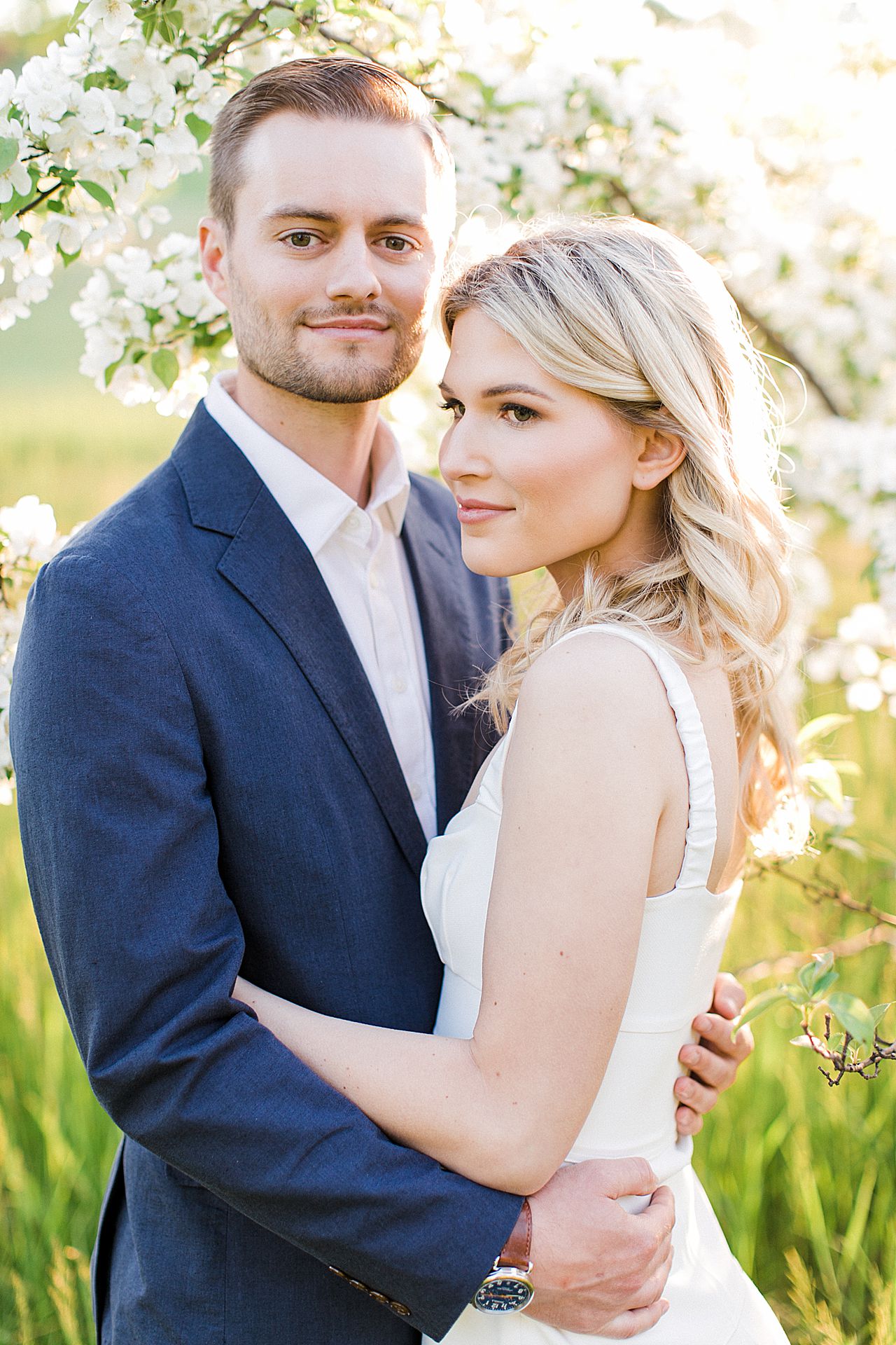 Engagement photos of a couple in a field with a blooming tree in the background in Northern Michigan