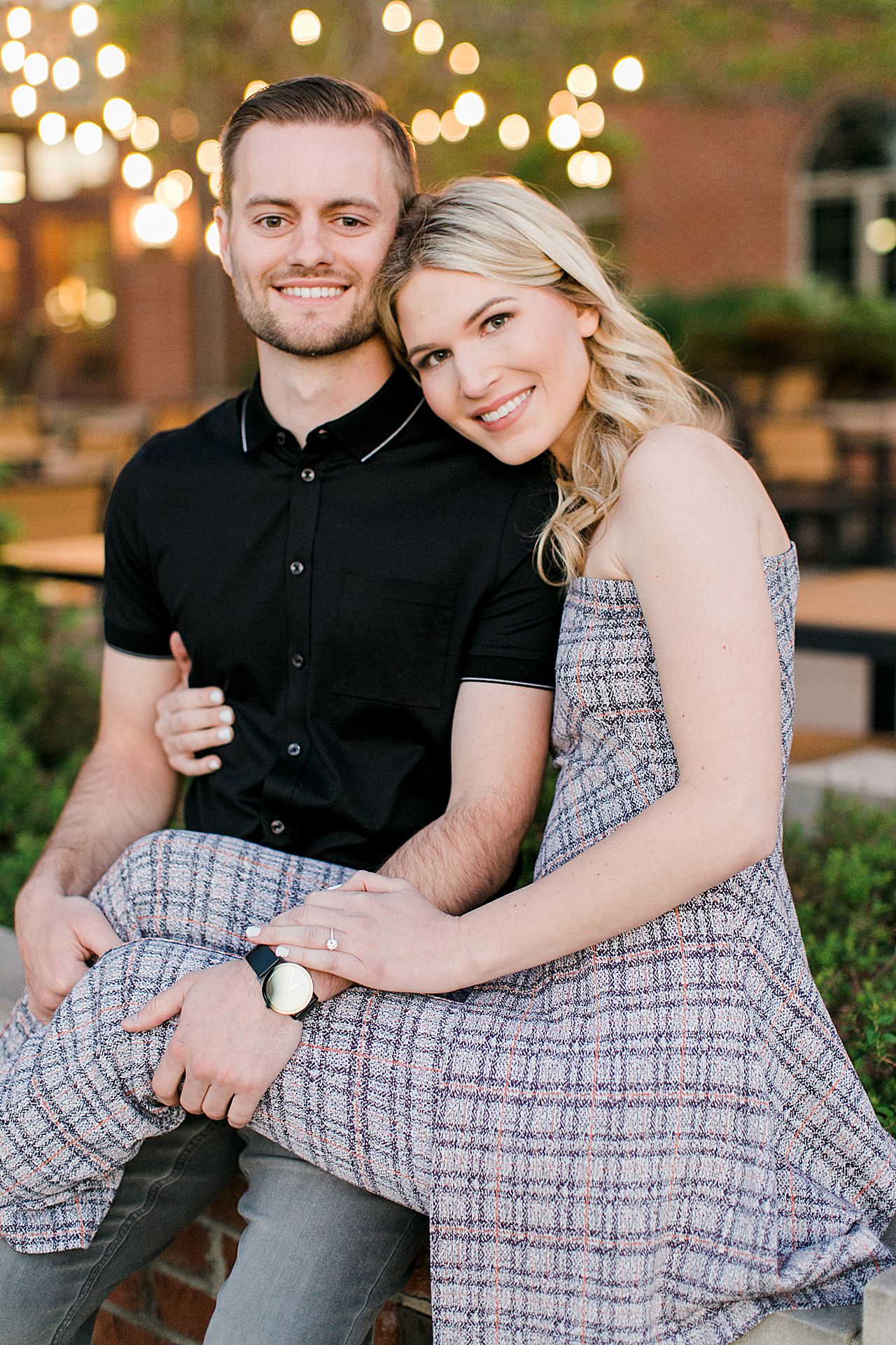 An engaged couple in Downtown Traverse City at dusk with a brick building and twinkle lights overhead
