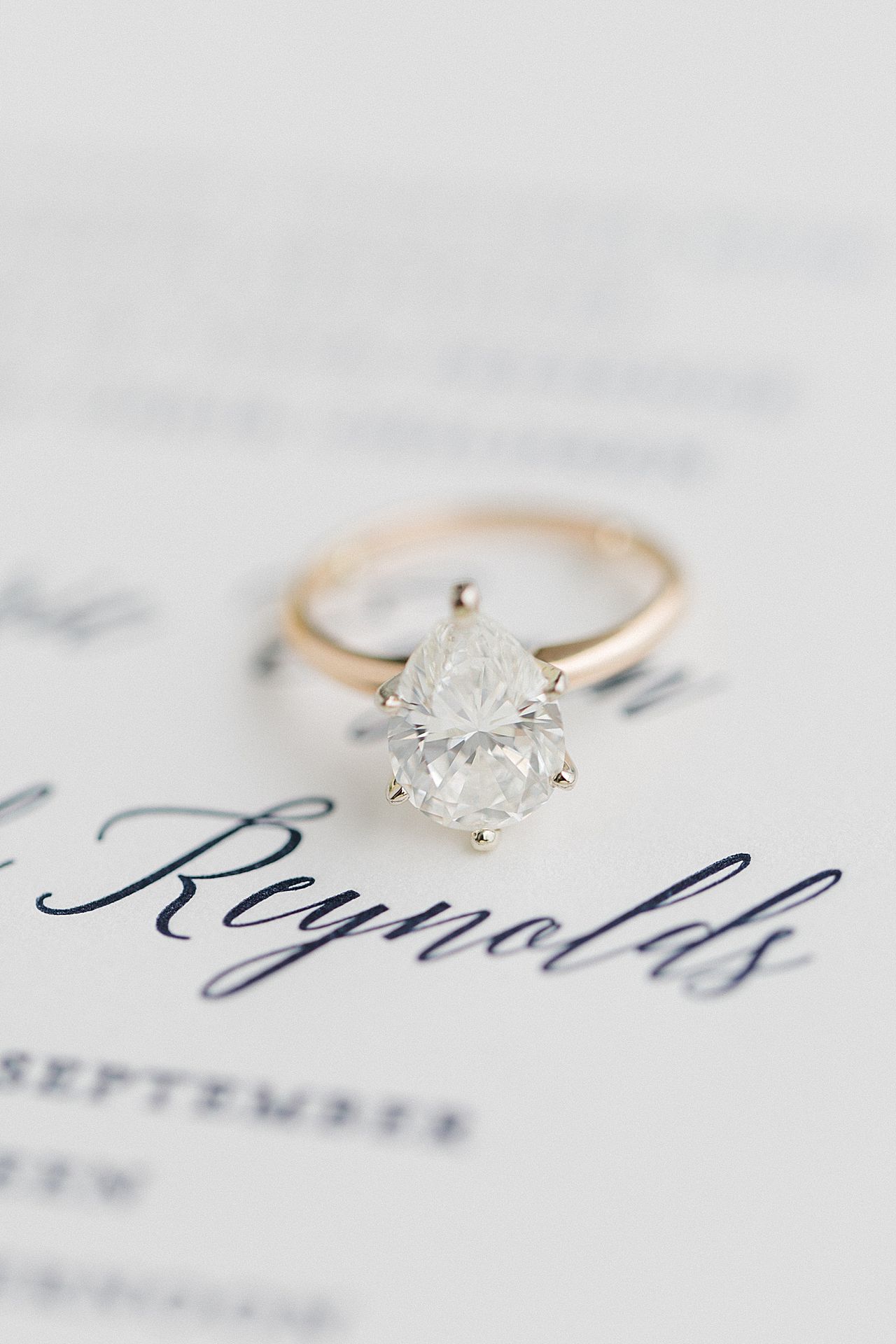 A brides pear shaped engagement ring on a wedding invitation