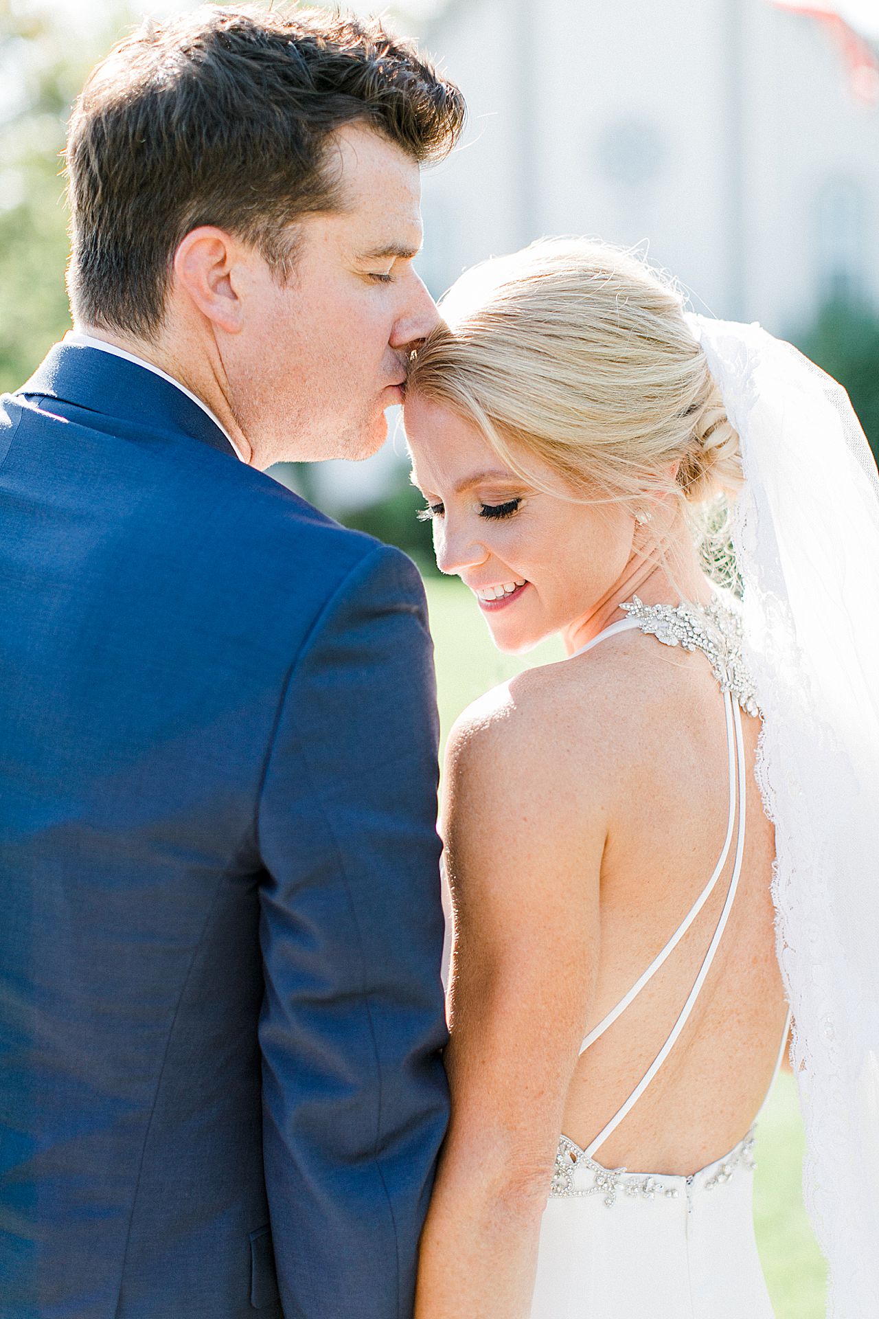 A groom kissing his brides forehead on a sunny day in Michigan