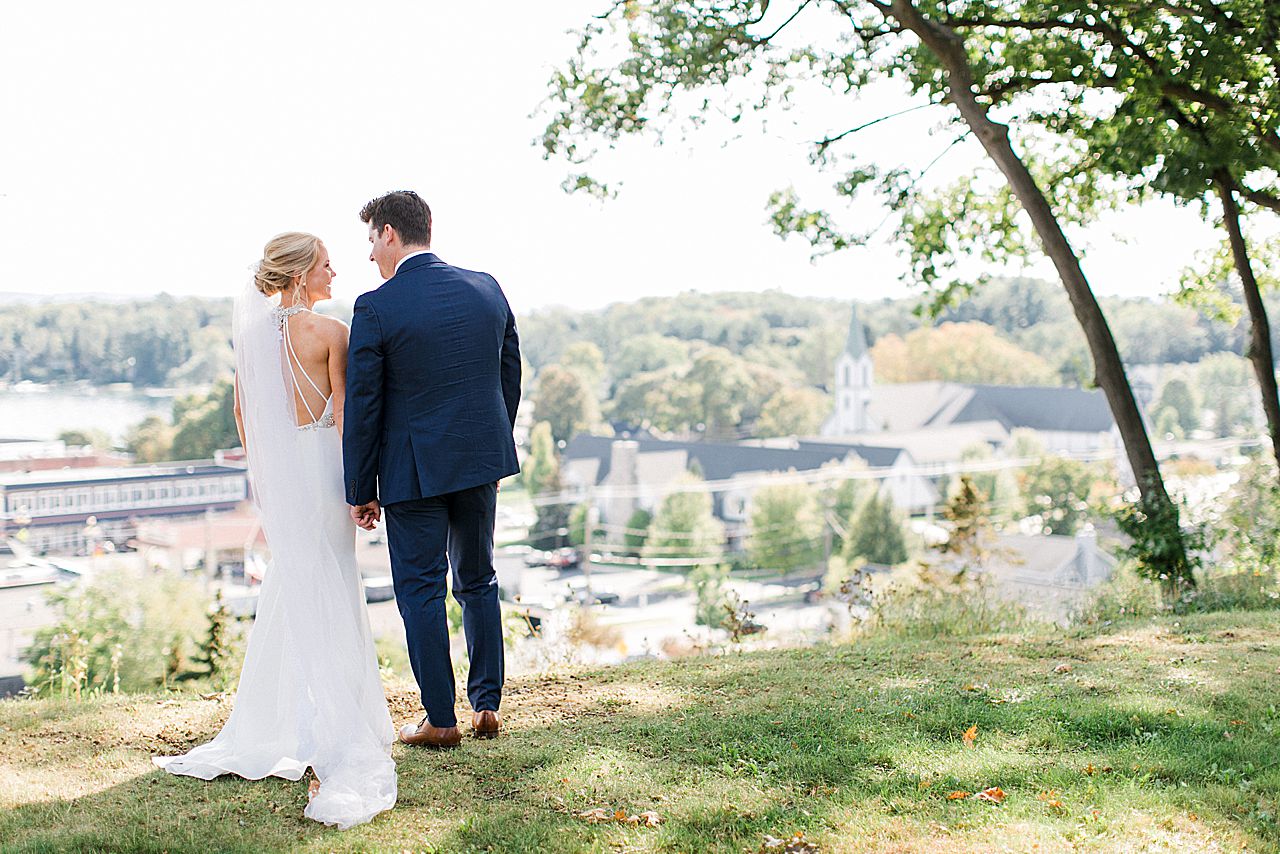 A bride and groom looking at the town of Harbor Springs, Michigan from an overlook after their wedding