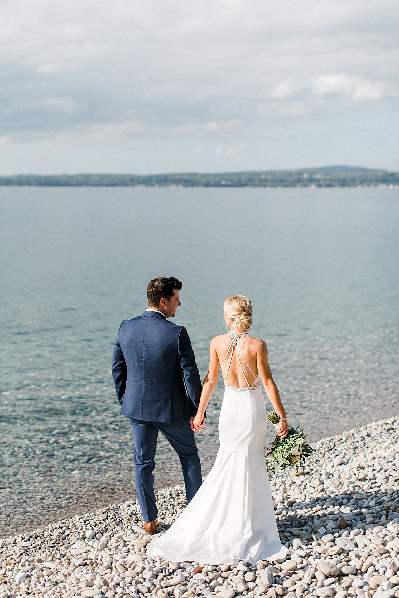 A portrait of a bride and groom holding hands on little traverse bay in Petoskey, Michigan