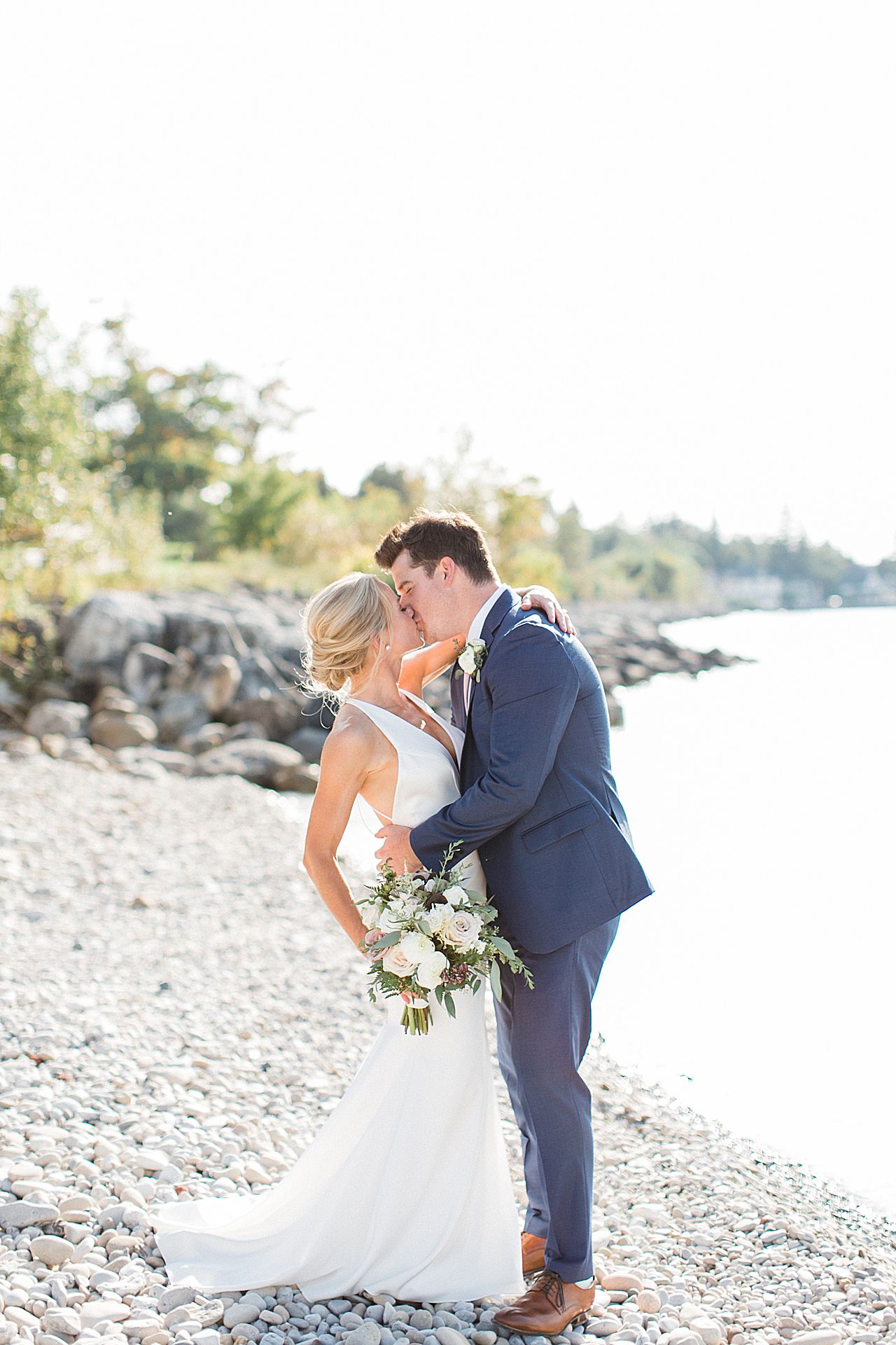 A portrait of a bride and groom kissing by the water in Petoskey, Michigan