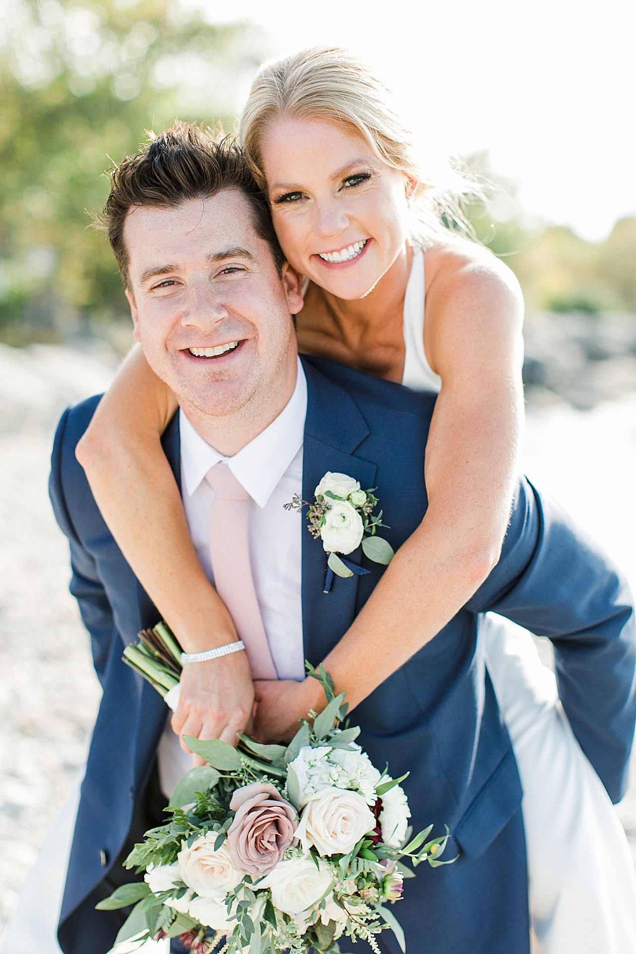A bride getting a piggy back ride from her groom by the lake in Michigan