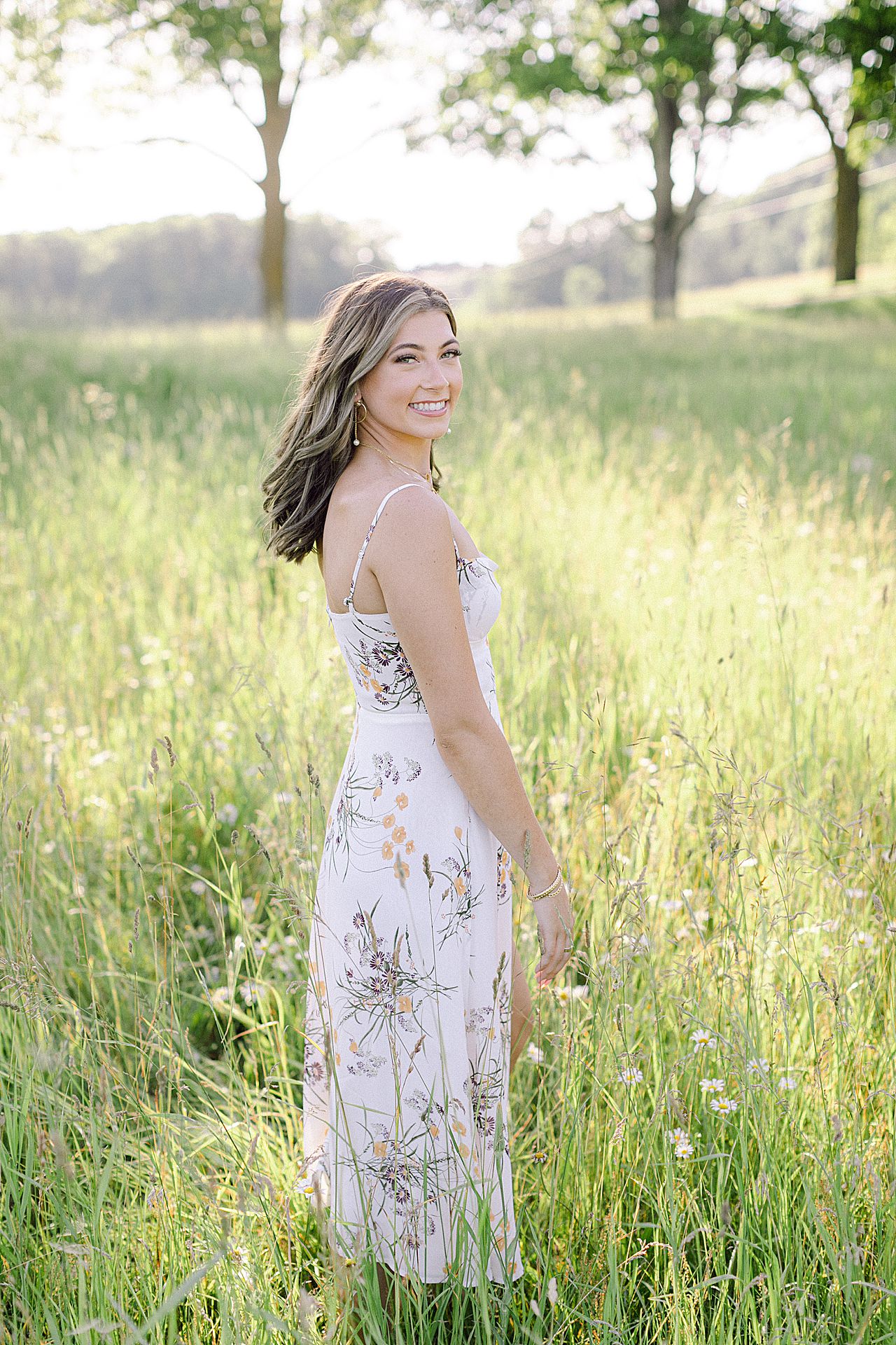 A high school senior girl walking tough a field while smiling on a sunny summer day in Northern Michigan