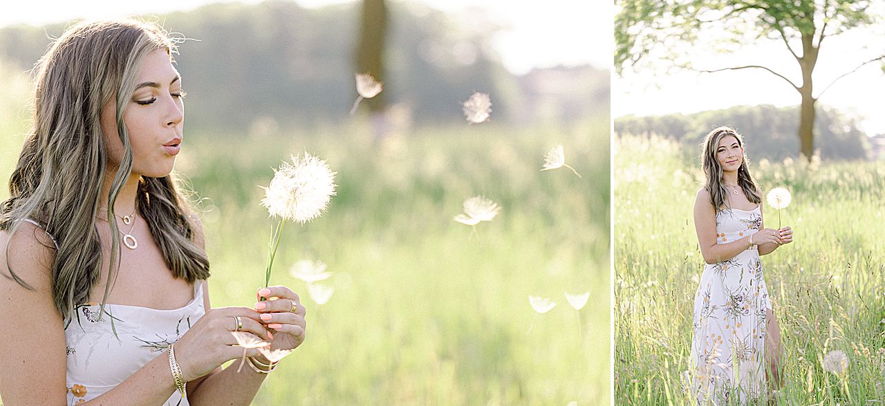 A high school senior girl holding a large dandelion and blowing the seeds into the wind in a field in Charlevoix, Michigan