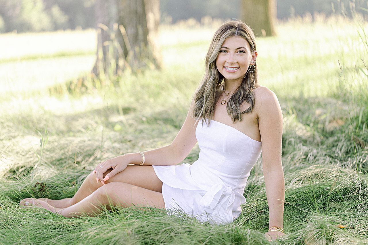 A girl taking senior portraits while sitting in a grassy field in Northern Michigan